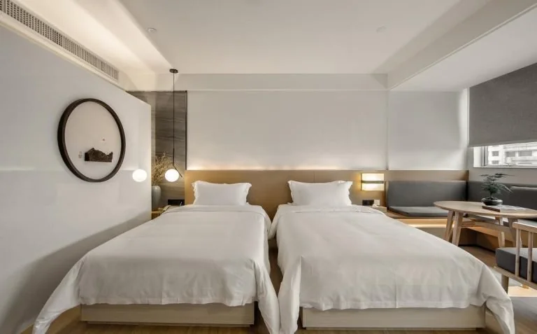 Twin hotel room with two beds, shared bedside table, desk and chairs