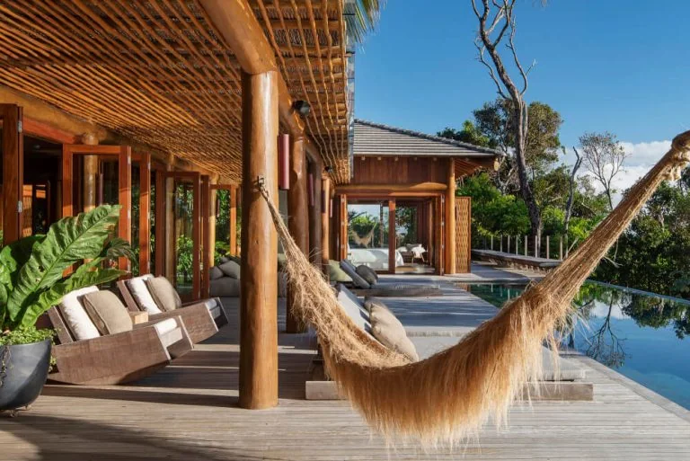 Covered outdoor resort lounge with sofas and chairs beside a pool