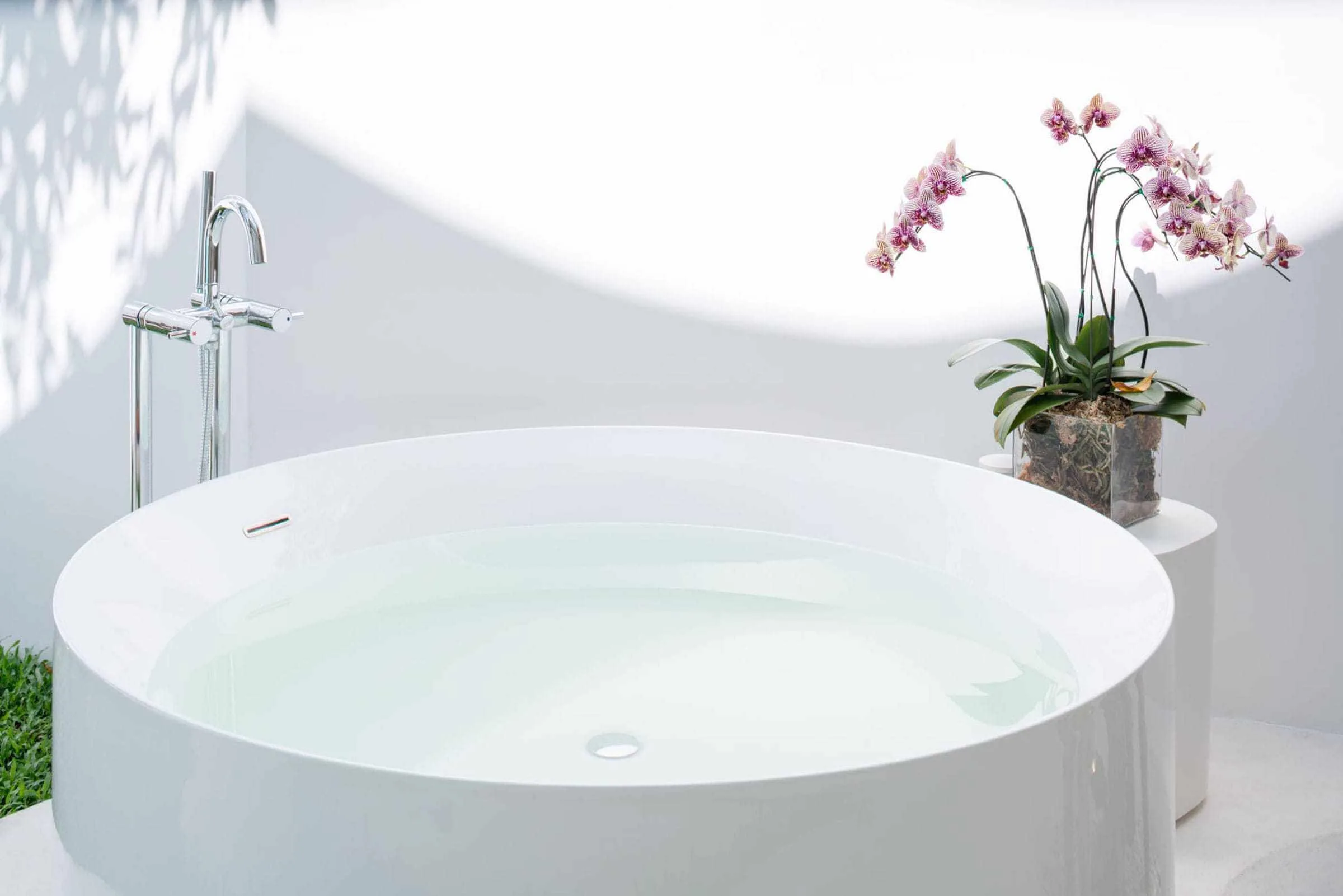 Round white bath on an open terrace with a small orchid arrangement