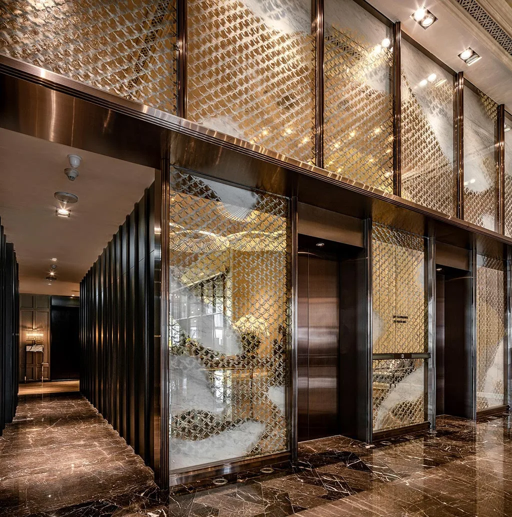 Hotel lift lobby with reflective metal screens, stone floor and lift doors