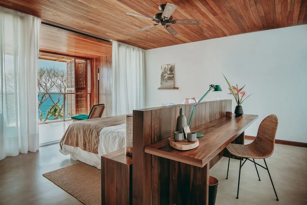 Guest room with timber ceiling, bed, desk and woven chair