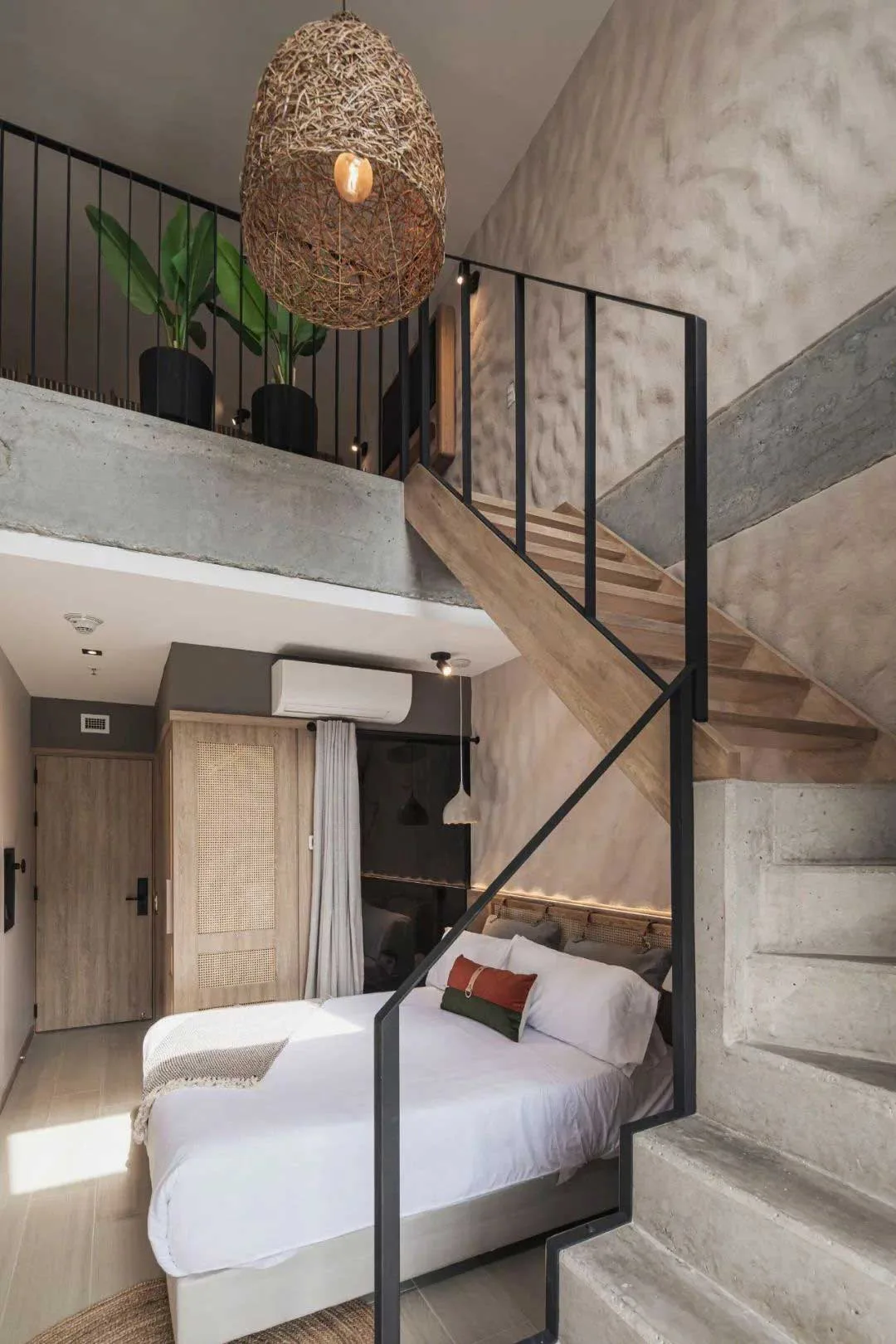 Duplex guest room with a bed, open stair and tall stone-toned wall