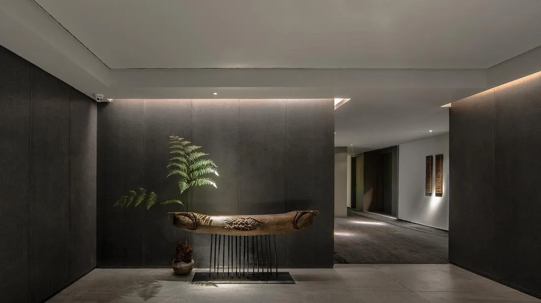 Hotel corridor with a narrow display console, linear lighting and a planted accent
