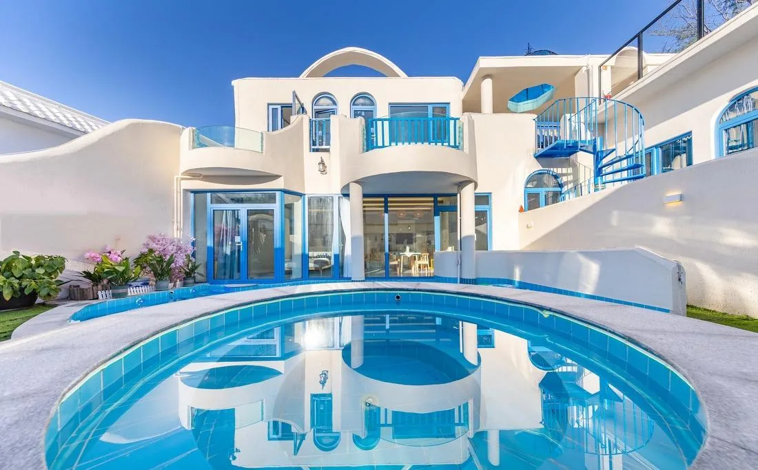 Curved resort pool in front of white guest buildings with blue trim