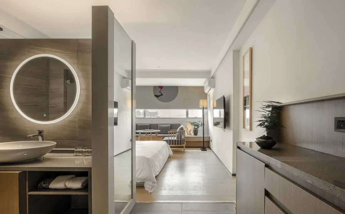 Guest-room entrance with open vanity, bed and timber-toned storage