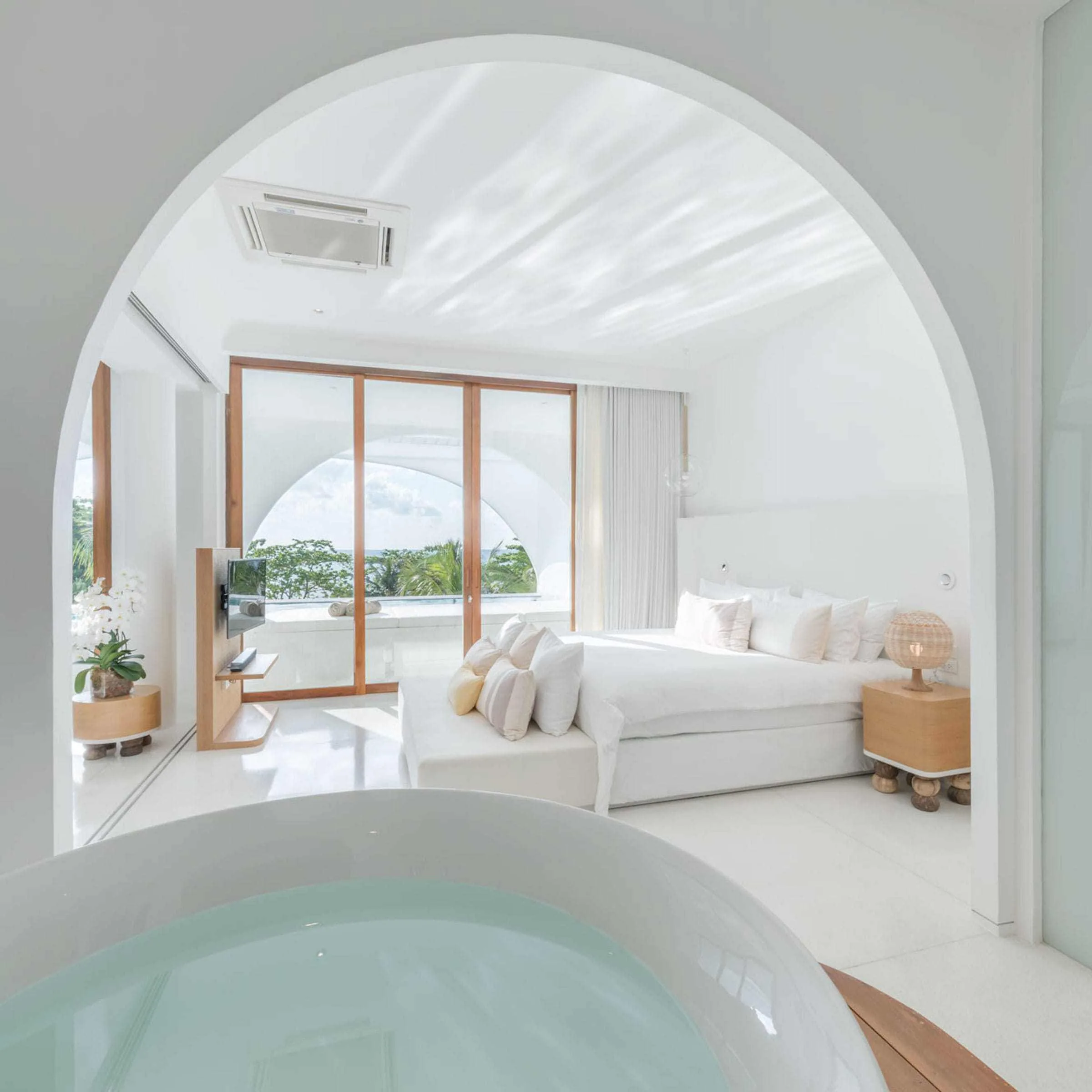 Guest suite with round bath, white seating and view toward the pool and beach