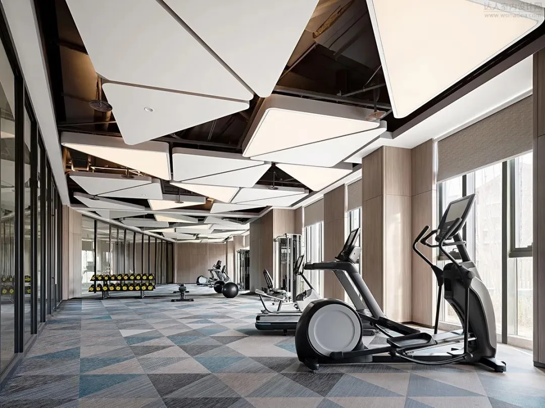 Hotel fitness room with cardio equipment and a geometric ceiling