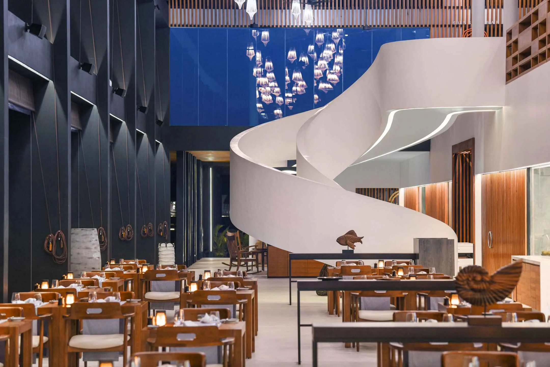 Resort restaurant with white stair, dark wall shelving and dining tables