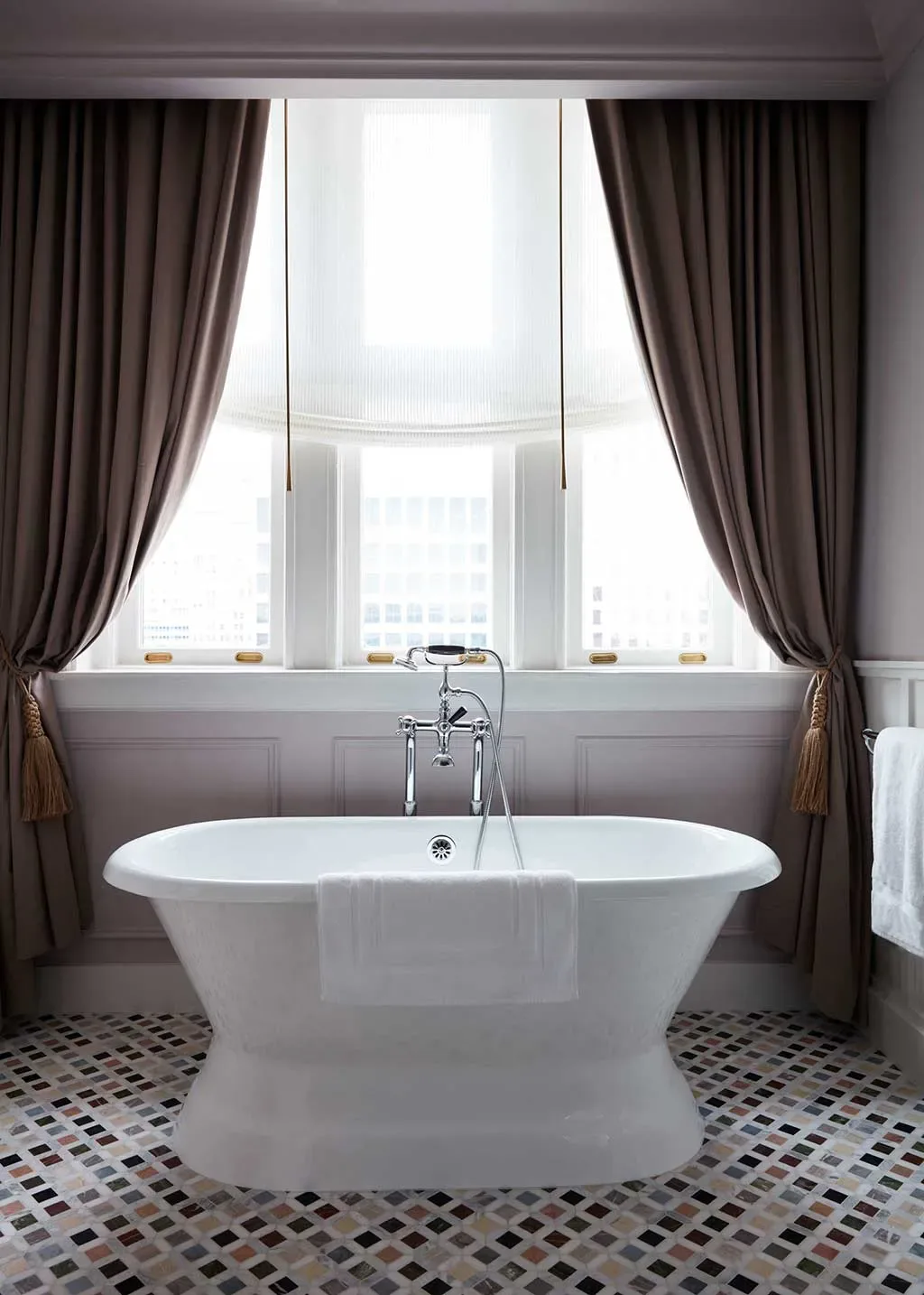 Freestanding bath set in front of a curtained guest-room window