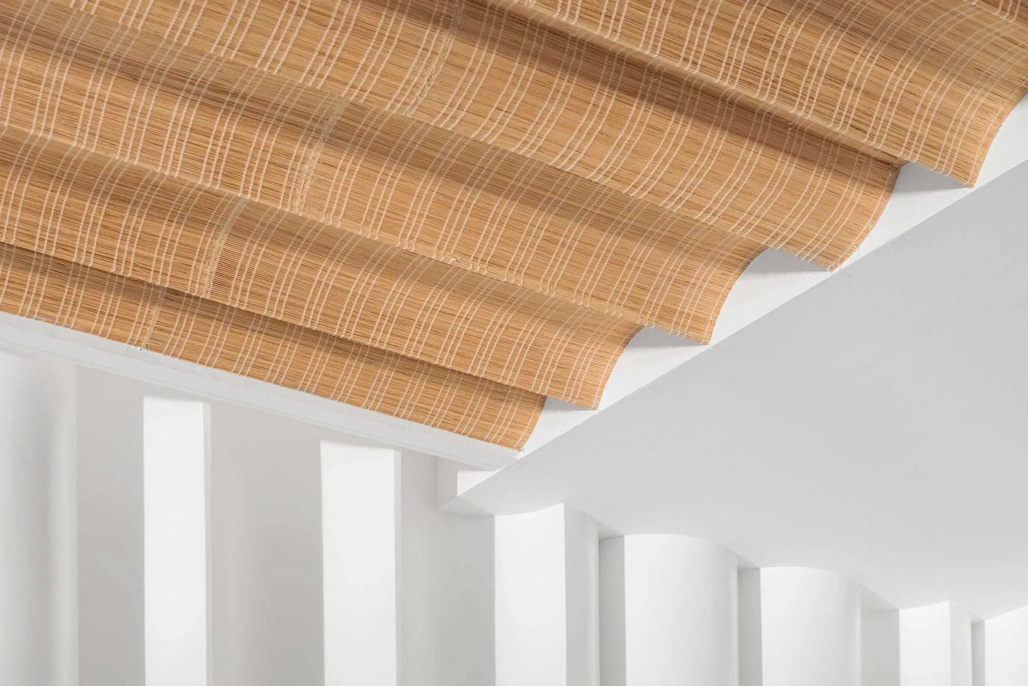 Woven ceiling shade above white columns and curved openings