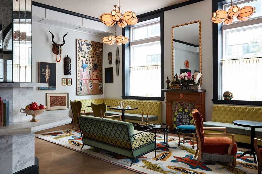 Boutique hotel lounge with patterned rugs, green sofas, armchairs, artwork and large windows