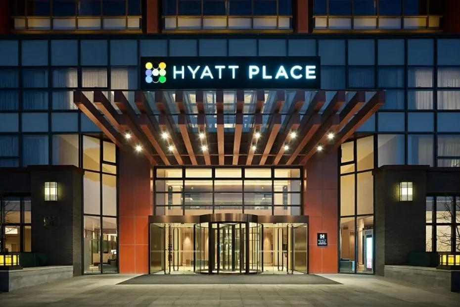Illuminated entrance of Beijing Hyatt Place with a glazed facade, hotel sign and timber-toned canopy