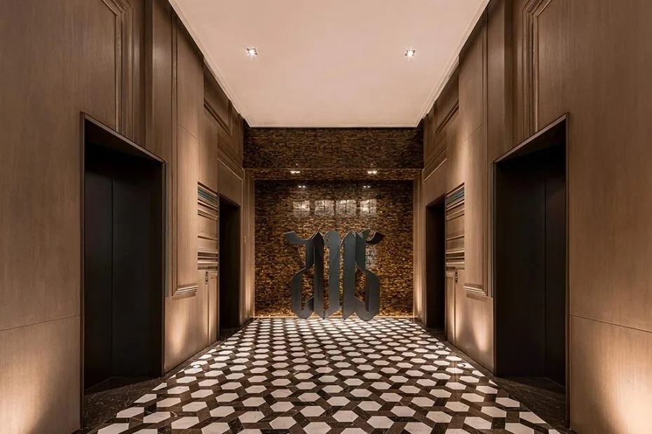 Hotel lift lobby with dark timber wall panels, patterned stone flooring and three lift doors