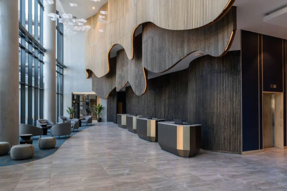 Contemporary hotel lobby with a tall dark feature wall, sculpted timber panels and reception desks